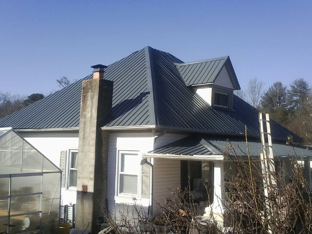 Dark blue standing seam metal roof on a white farmhouse with dormer — Slate & Tile Roof Repair by Roofing Brothers in Lodge
