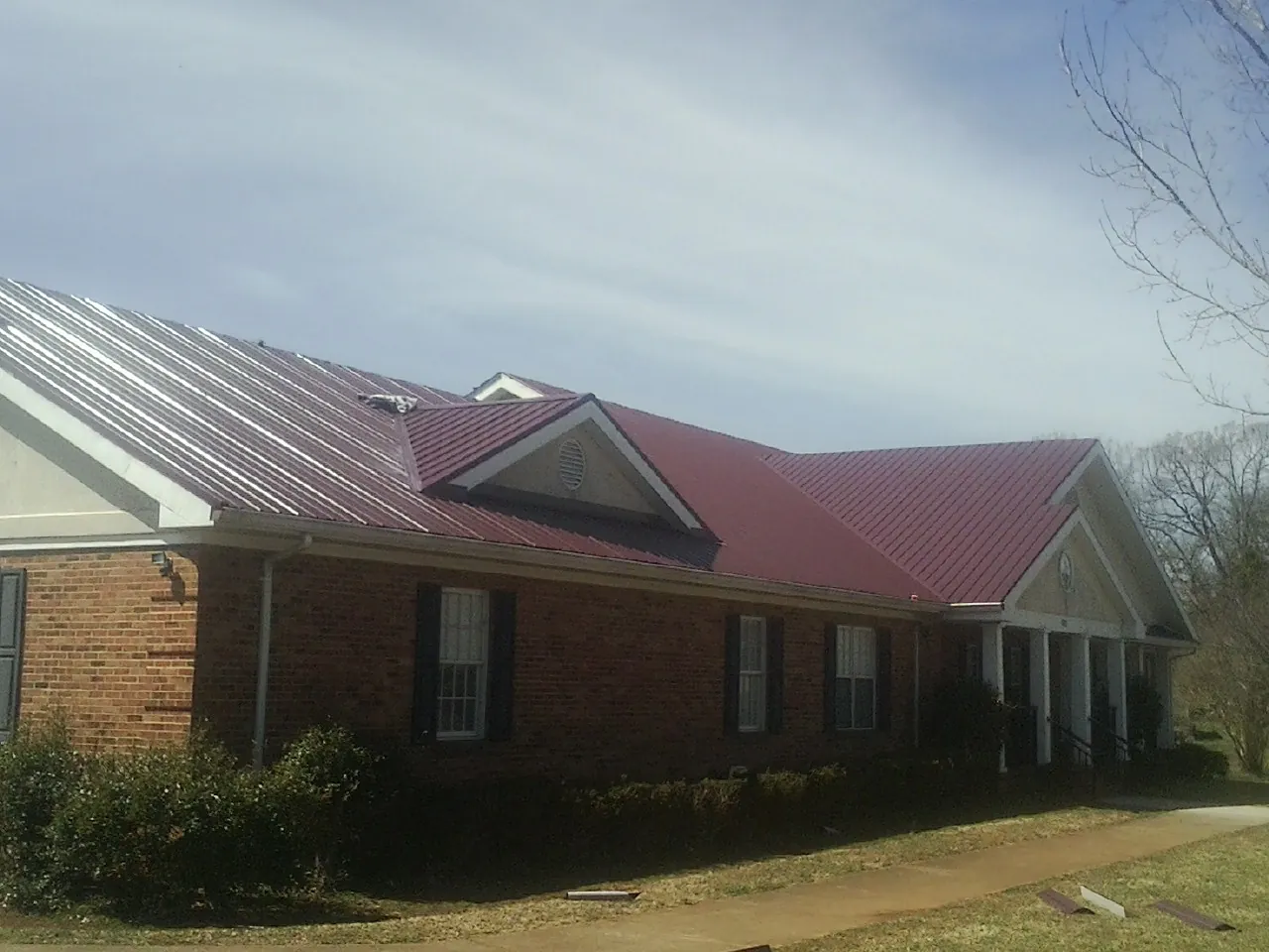 Red metal roof with gabled entries on a long brick building, from a Hail Damage Roof Repair job in Lodge