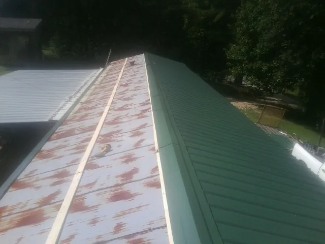 Old rusted panels beside newly installed green metal roofing — Wind Damage Roof Repair by Roofing Brothers in Lodge