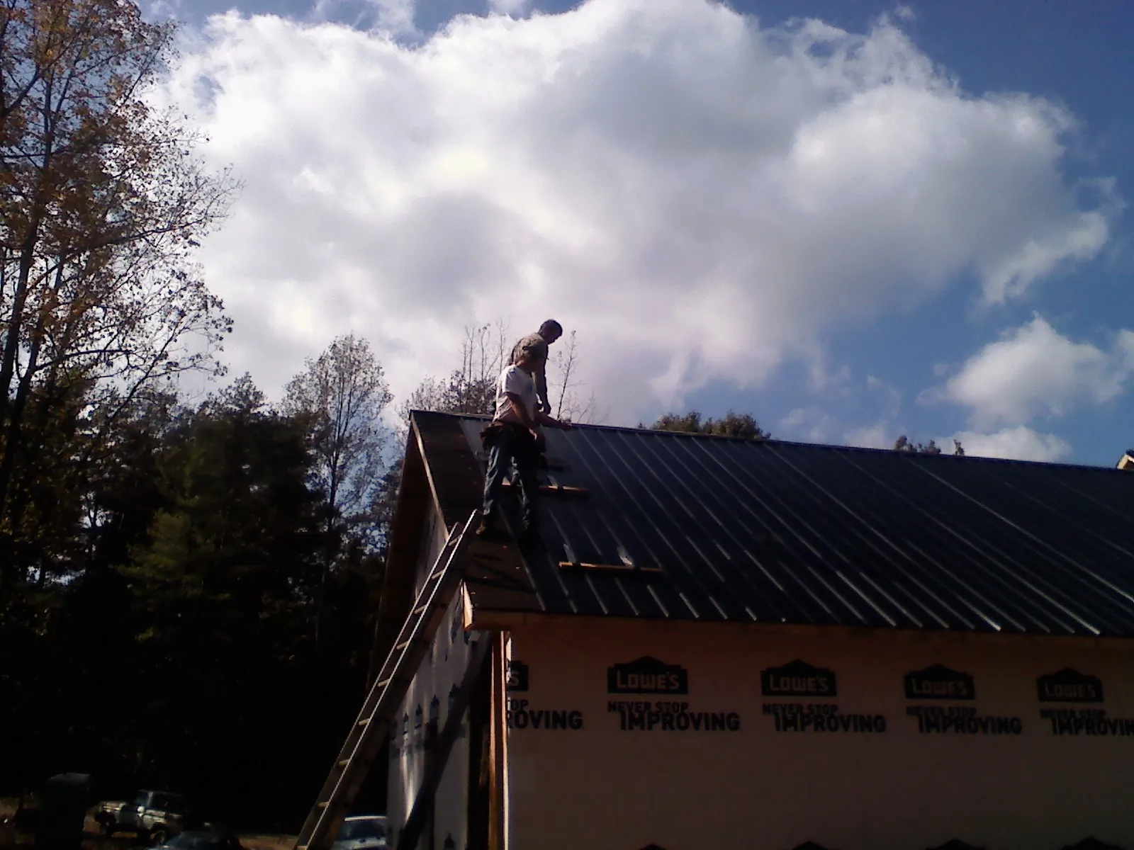 Roofer fastening dark metal panels high against a cloudy sky, from a Roof Inspection job in Lodge